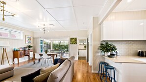A modern kitchen with white cabinets, a wooden countertop, and blue bar stools. - Keeler Cottage (East Toowoomba)