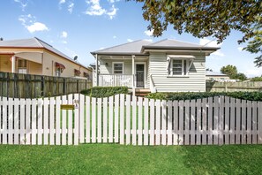 A single-story house with a white picket fence, a front porch, and a well-maintained lawn. - Keeler Cottage (East Toowoomba)
