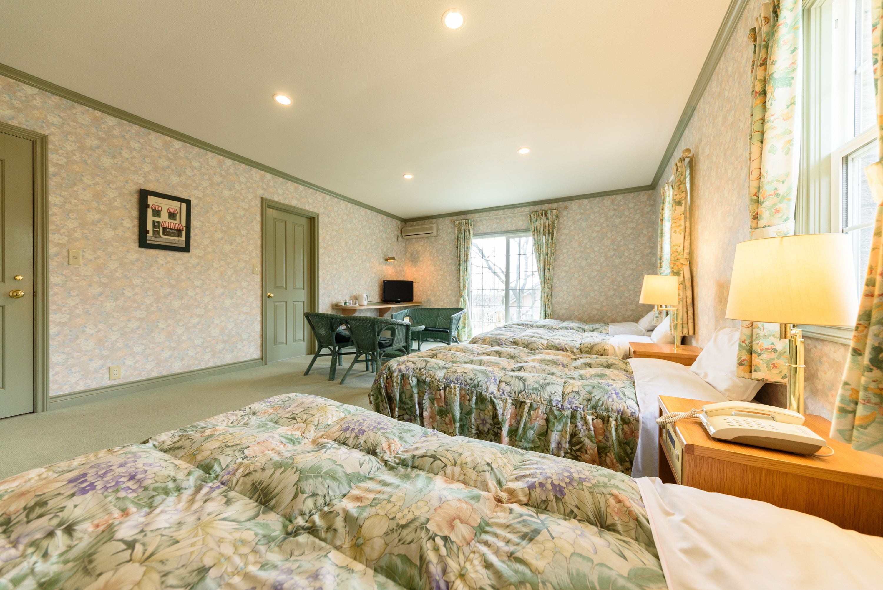 A hotel room with floral-patterned beds, a desk, and a chair.