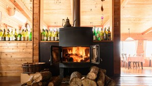 Un poêle à bois sur lequel repose une théière, entouré de bois de chauffage empilé et de bouteilles de vin disposées sur des étagères.