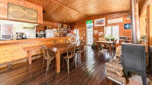 Un intérieur en bois comprenant un coin bar, une table à manger, des chaises et un poêle à bois.