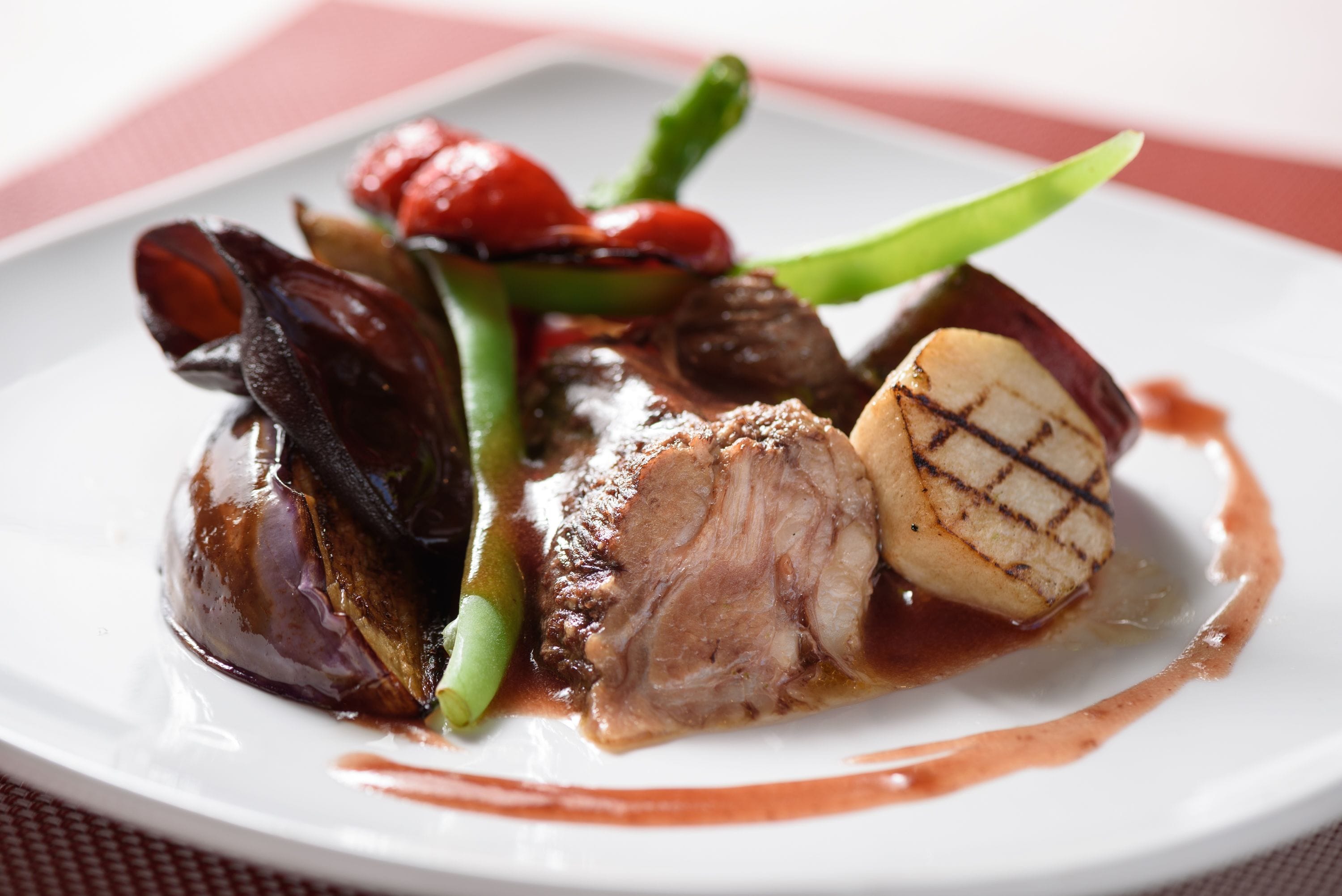 Une assiette de nourriture comprenant de la viande grillée, des légumes et une sauce.