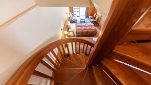 Un escalier en colimaçon en bois mène à une chambre à coucher qui contient un lit, une petite table et deux chaises.