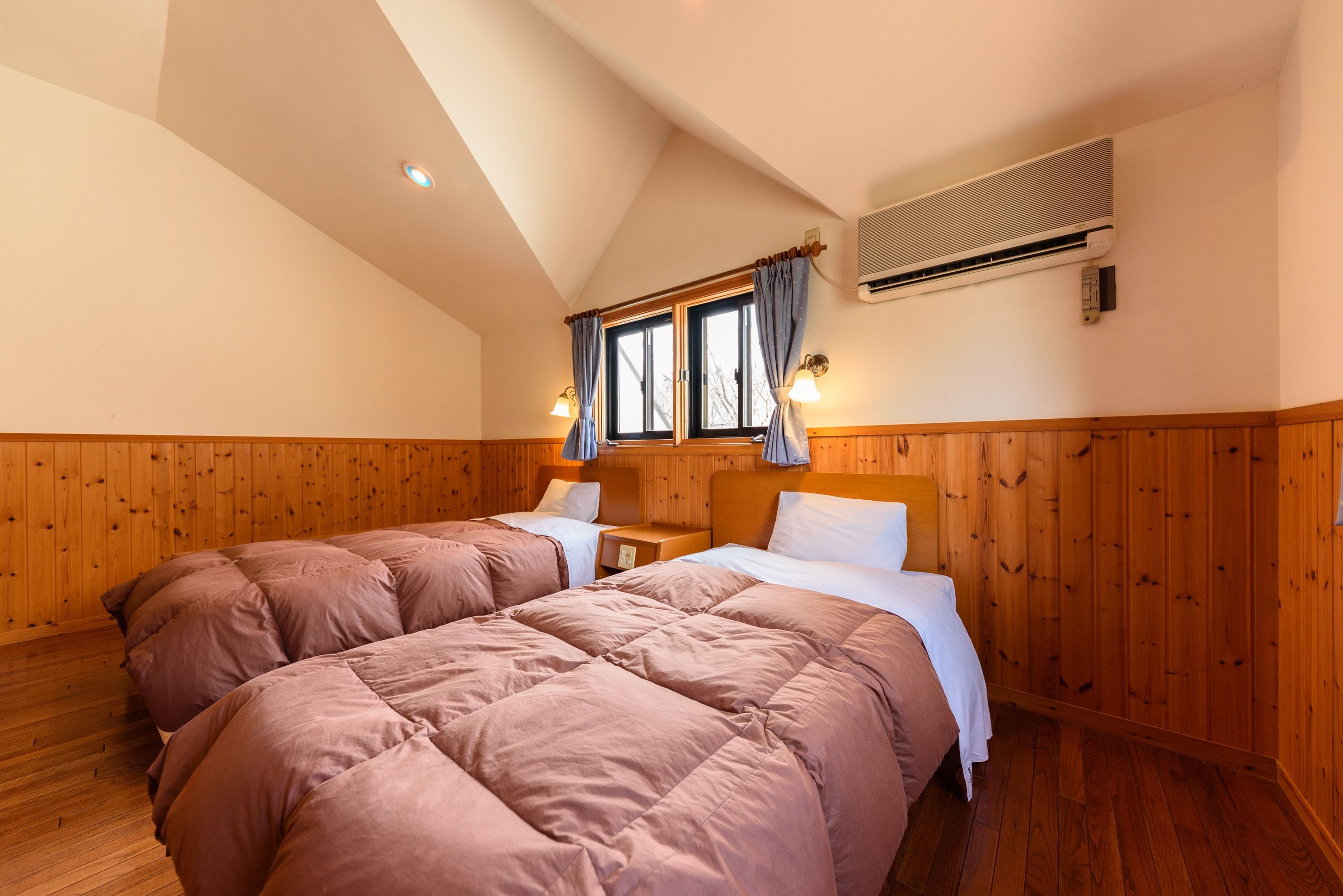 A bedroom with two beds, wooden walls, a sloped ceiling, and an air conditioning unit.