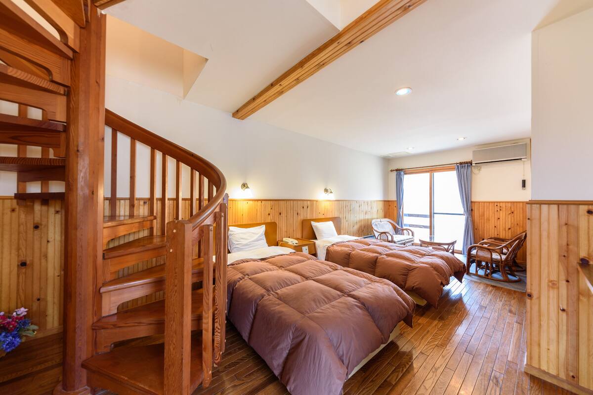 Una escalera de madera que conduce a un dormitorio con dos camas, una silla y un sillón mecedora.