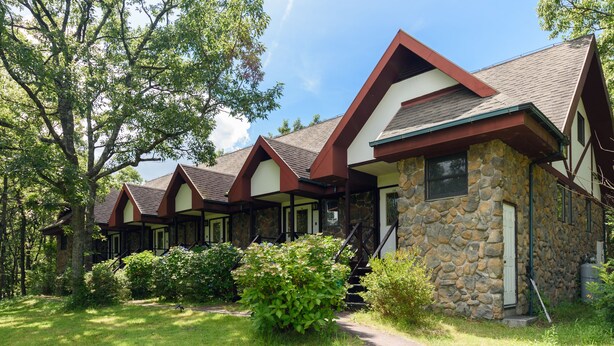 Une rangée de cabanes en pierre et en bois, dotées de toits à deux versants, entourées d’une végétation luxuriante.