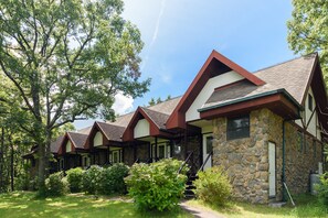 Une rangée de cabanes en pierre et en bois, dotées de toits à deux versants, entourées d’une végétation luxuriante.