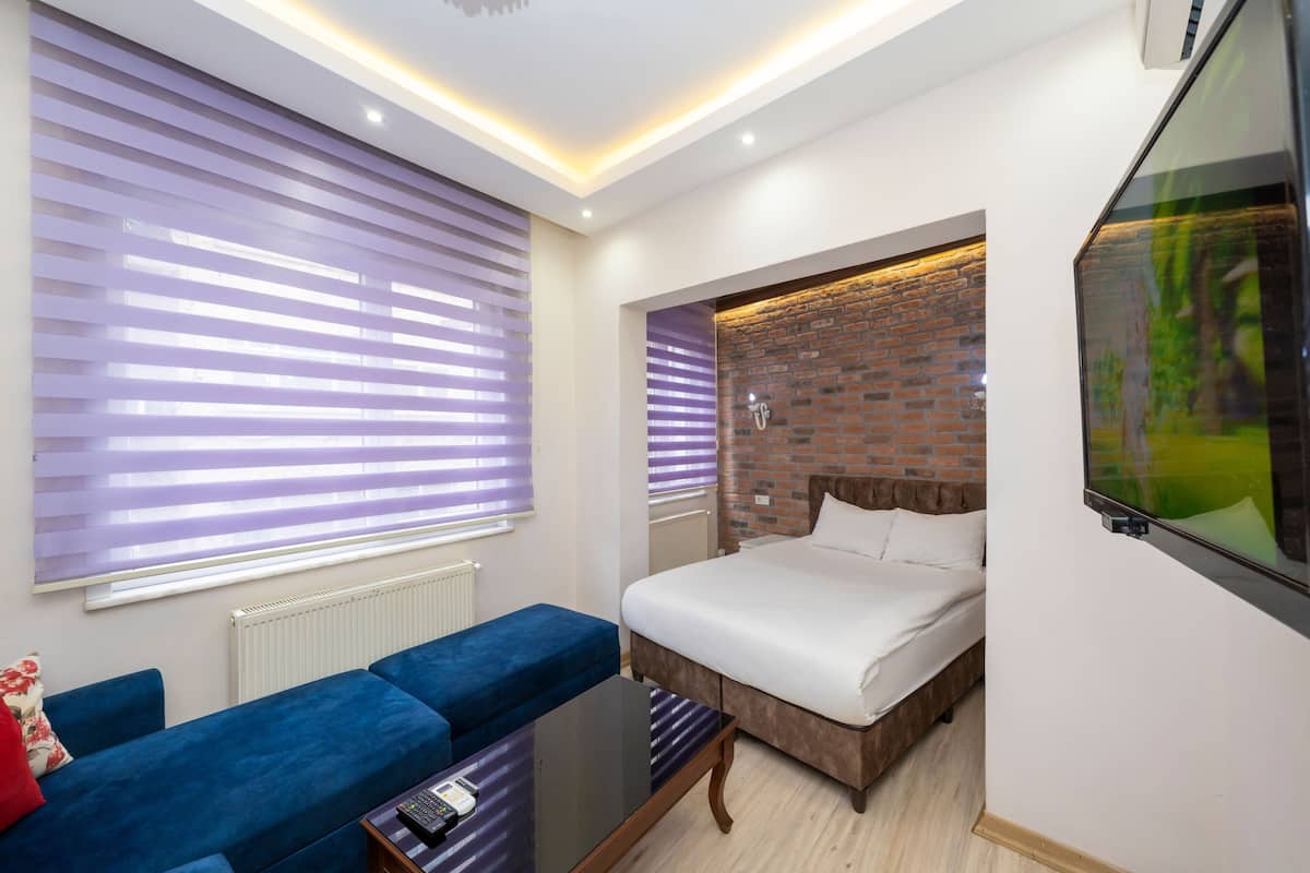 A modern hotel room with a bed, a blue sofa, a glass coffee table, and a TV mounted on the wall.
