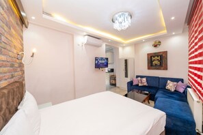 A modern bedroom with a bed, a blue sofa, a chandelier, and a TV. - Taksim City Suites (Istanbul)
