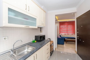A modern kitchen with white cabinets, a black countertop, and a double sink. A microwave is on the counter, and there is a small wooden table with a blue chair in the background. - Taksim City Suites (Istanbul)