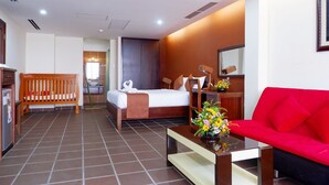 Ein Hotelzimmer mit einem Bett, einem roten Sofa, einer Holzbank, einem kleinen Tisch mit Blumenvase und einem im Hintergrund sichtbaren Badezimmer.