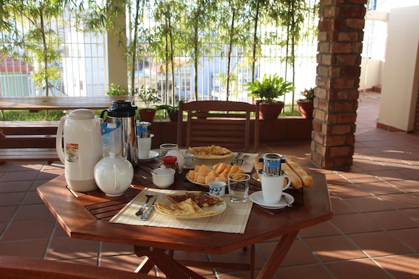 Una mesa de desayuno con cafetera, tetera, tazas y platos con comida.