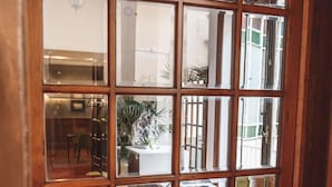 Une porte à ossature en bois, dotée de panneaux de verre, qui donne sur un espace intérieur avec un parquet en point de Hongrie, un coin repas et une vue sur l’extérieur.