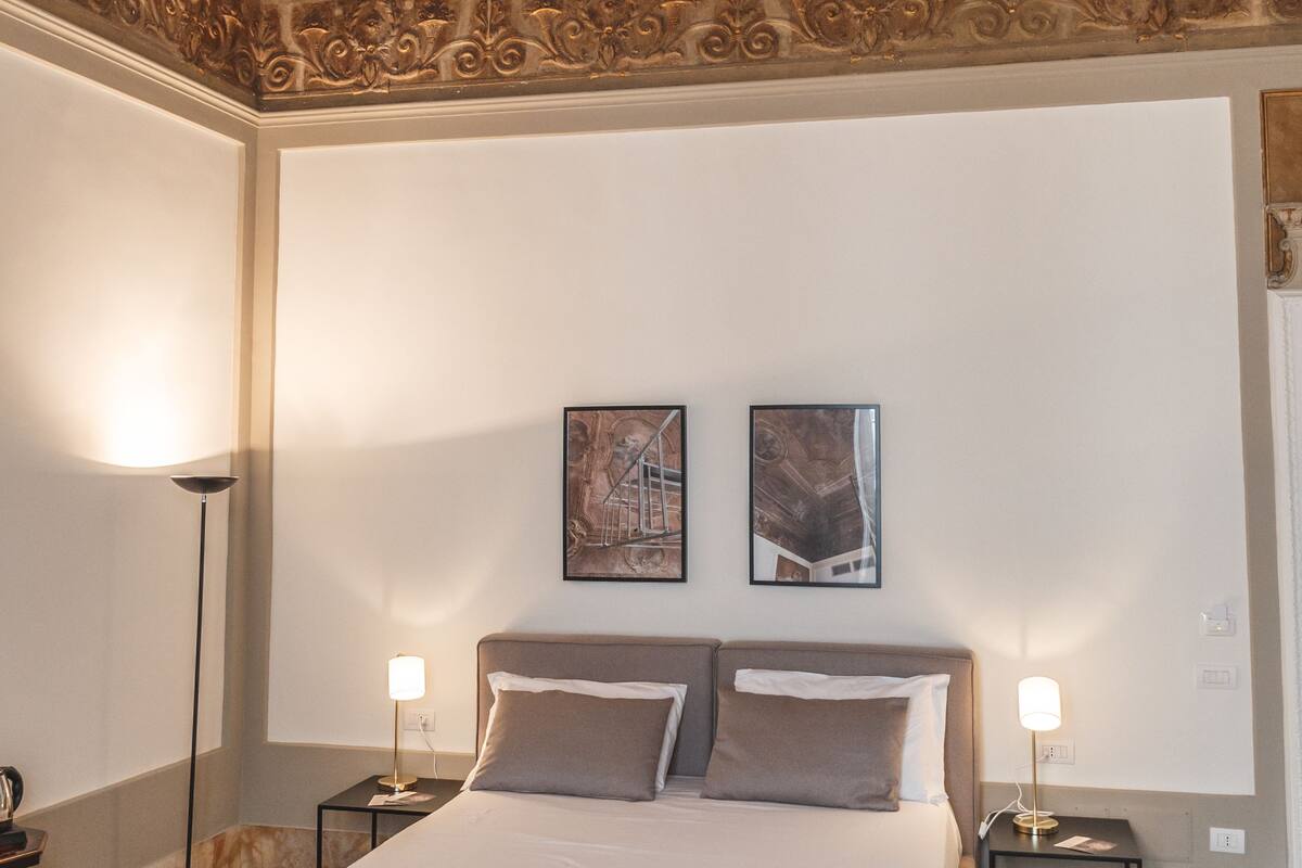 Ett hotellrum med en stor säng, två sängbord, en golvlampa och ett tak med detaljerad konstutsmyckning.