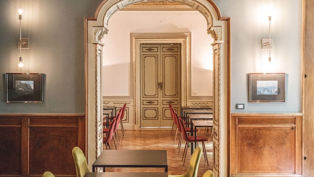 Un espace repas avec des tables et des chaises, une porte en arc de cercle et des tableaux encadrés accrochés aux murs.