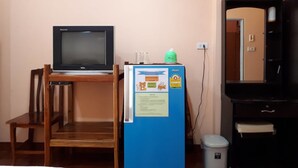 Una habitación con una televisión sobre un mueble de madera, un refrigerador azul con un aviso, una silla y un cesto de basura.