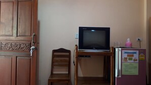 Una habitación con puerta de madera, televisor sobre un mueble, una silla y un refrigerador con un aviso.