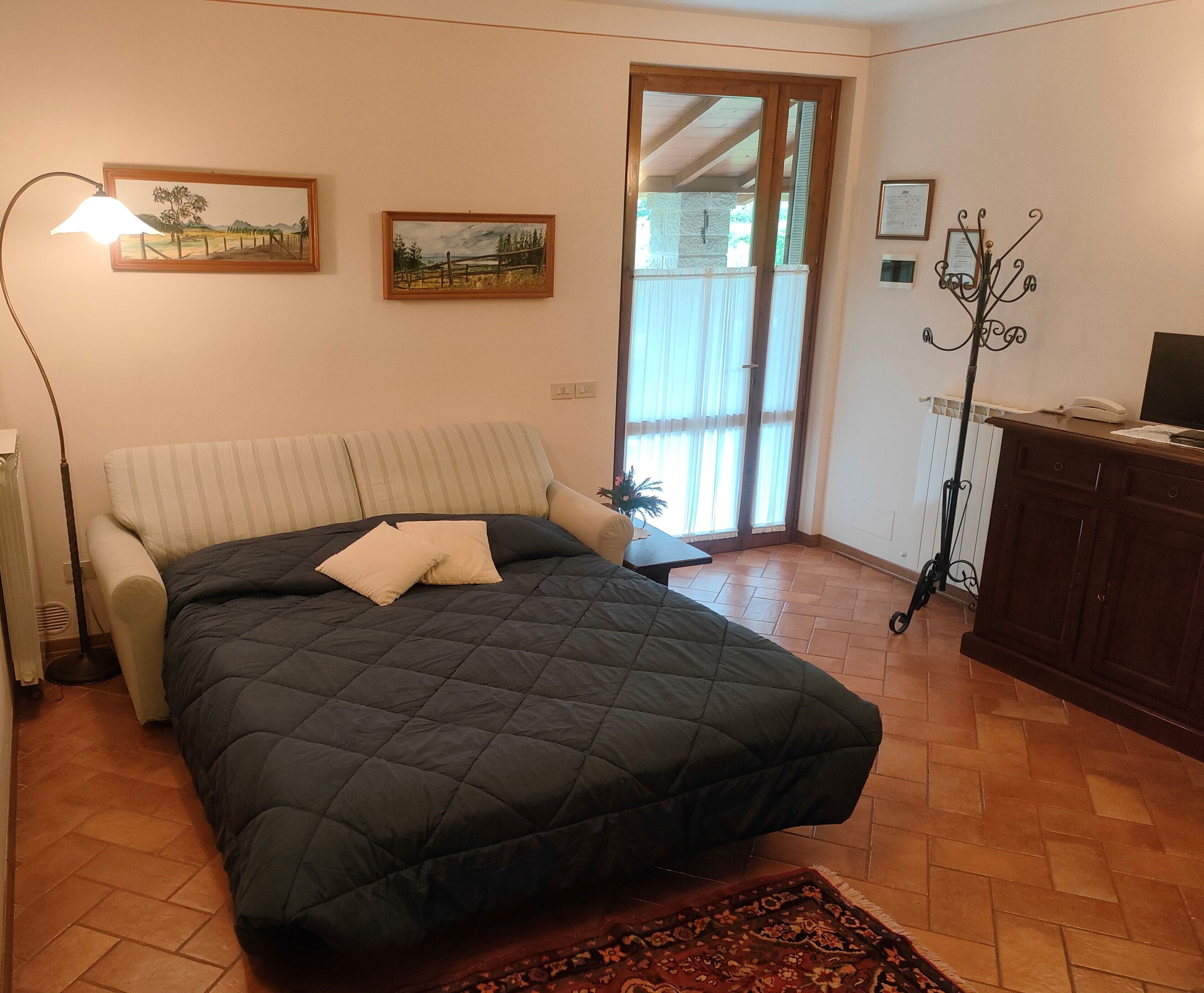 Een slaapkamer met een bed, een lamp, een radiator, een houten kast en een raam met gordijnen.