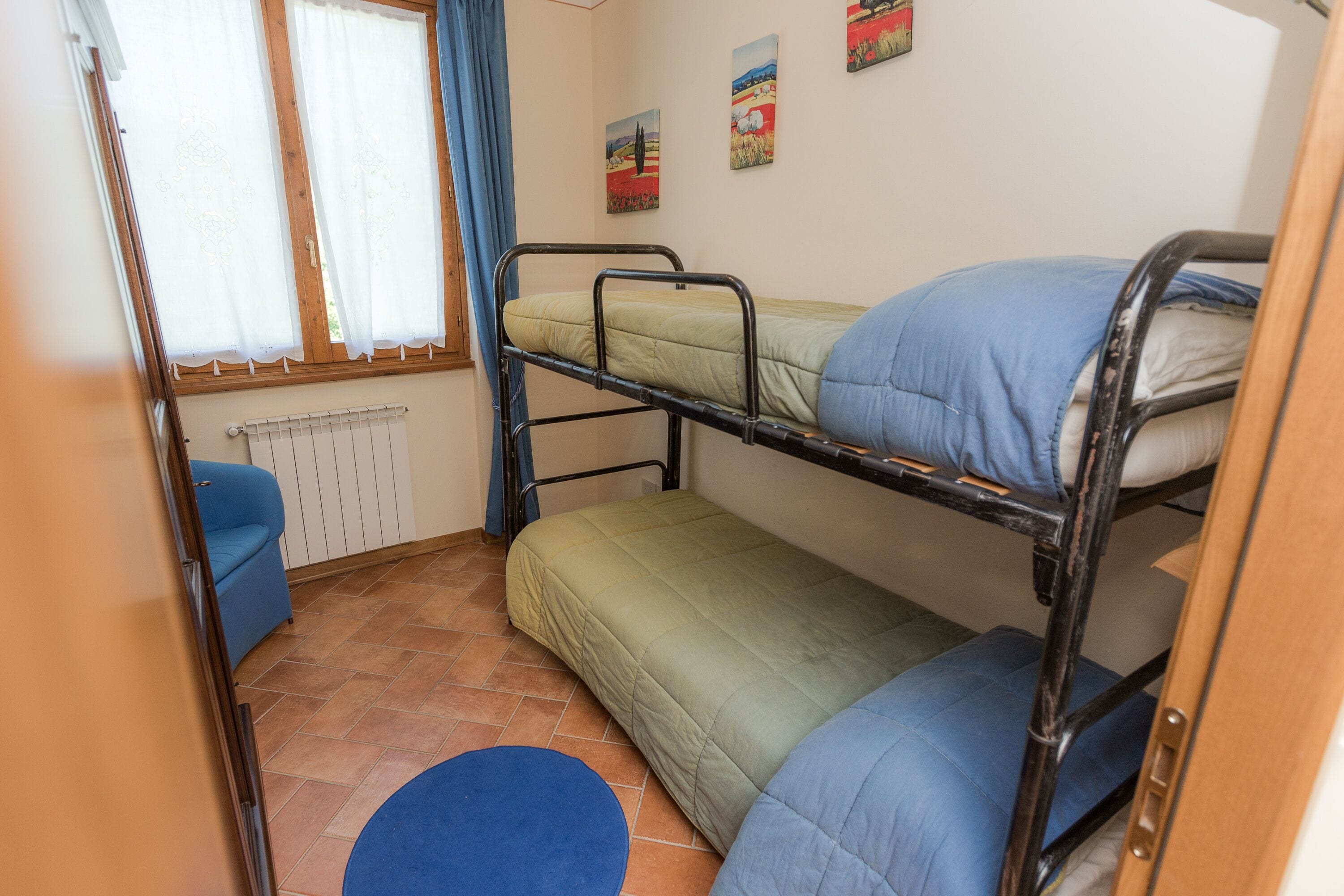 A bunk bed room with a blue chair, a radiator, and artwork on the wall.