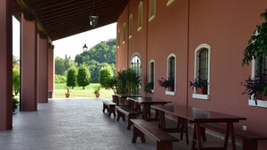 Eine überdachte Terrasse im Freien mit Holzbänken und -tischen, Blumentöpfen und Blick auf eine grüne Landschaft.