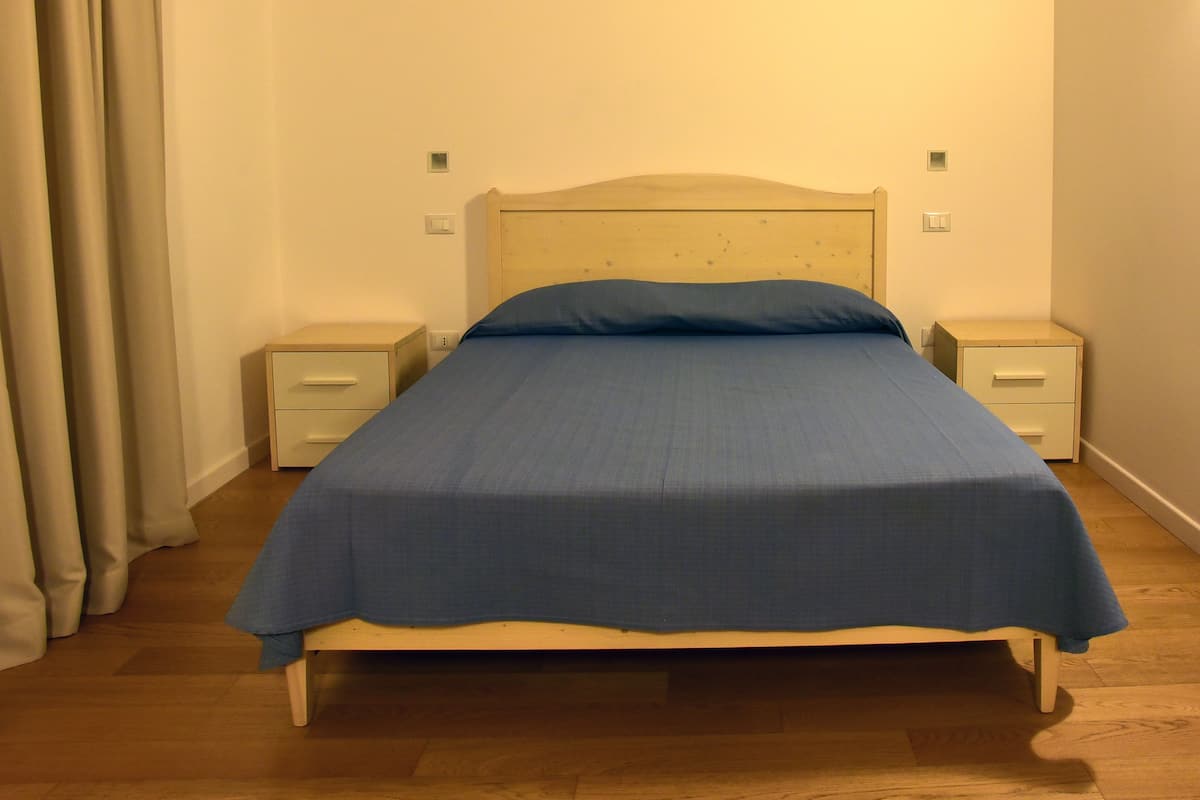 Una cama individual con cabecera de madera, una colcha azul y dos mesitas de noche con cajones.