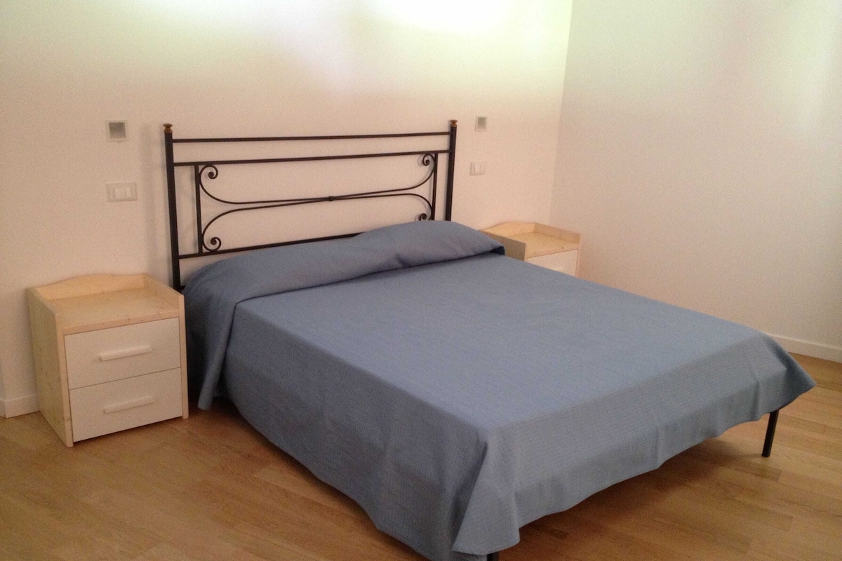 Una cama individual con cabecera metálica, dos mesitas de noche y suelo de madera.