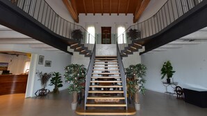 Ein großzügiger Innenraum mit einer zentralen Treppe, Holzbalken an der Decke und Topfpflanzen.