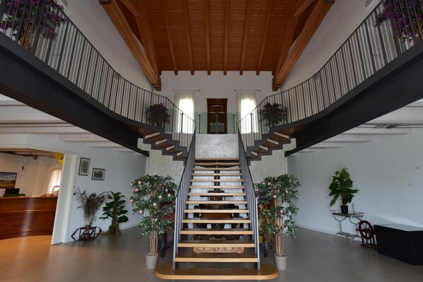 A spacious interior with a central staircase, wooden ceiling beams, and potted plants. - Tenuta Monterosso (Teolo)