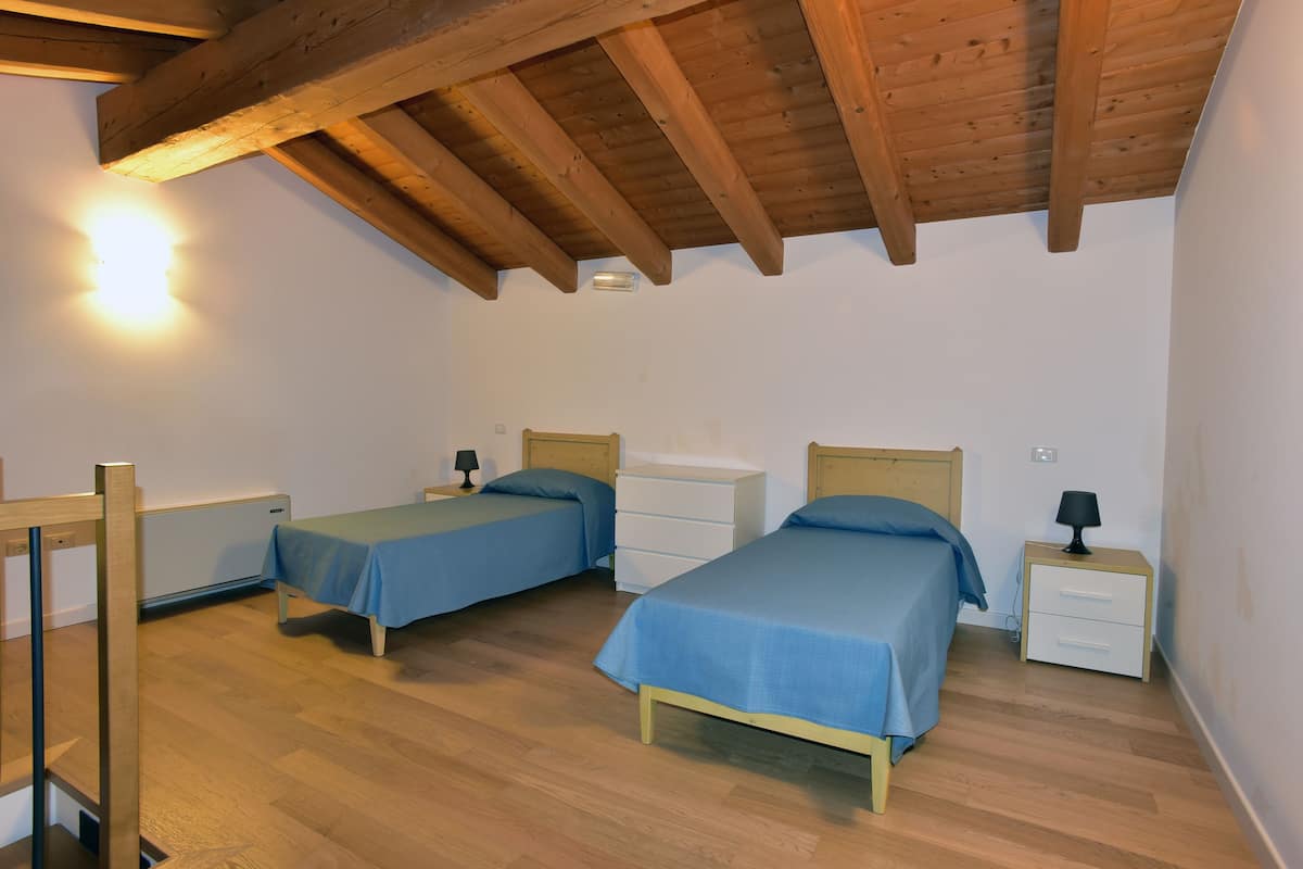 Un dormitorio con dos camas individuales, cabeceros de madera, mesitas de noche con lámparas y techo de madera.