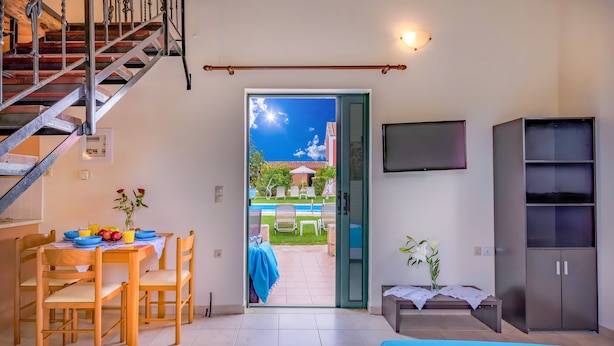 A room with a bed, a dining table with chairs, a TV mounted on the wall, and a staircase. - Athousakis Village (Chania)