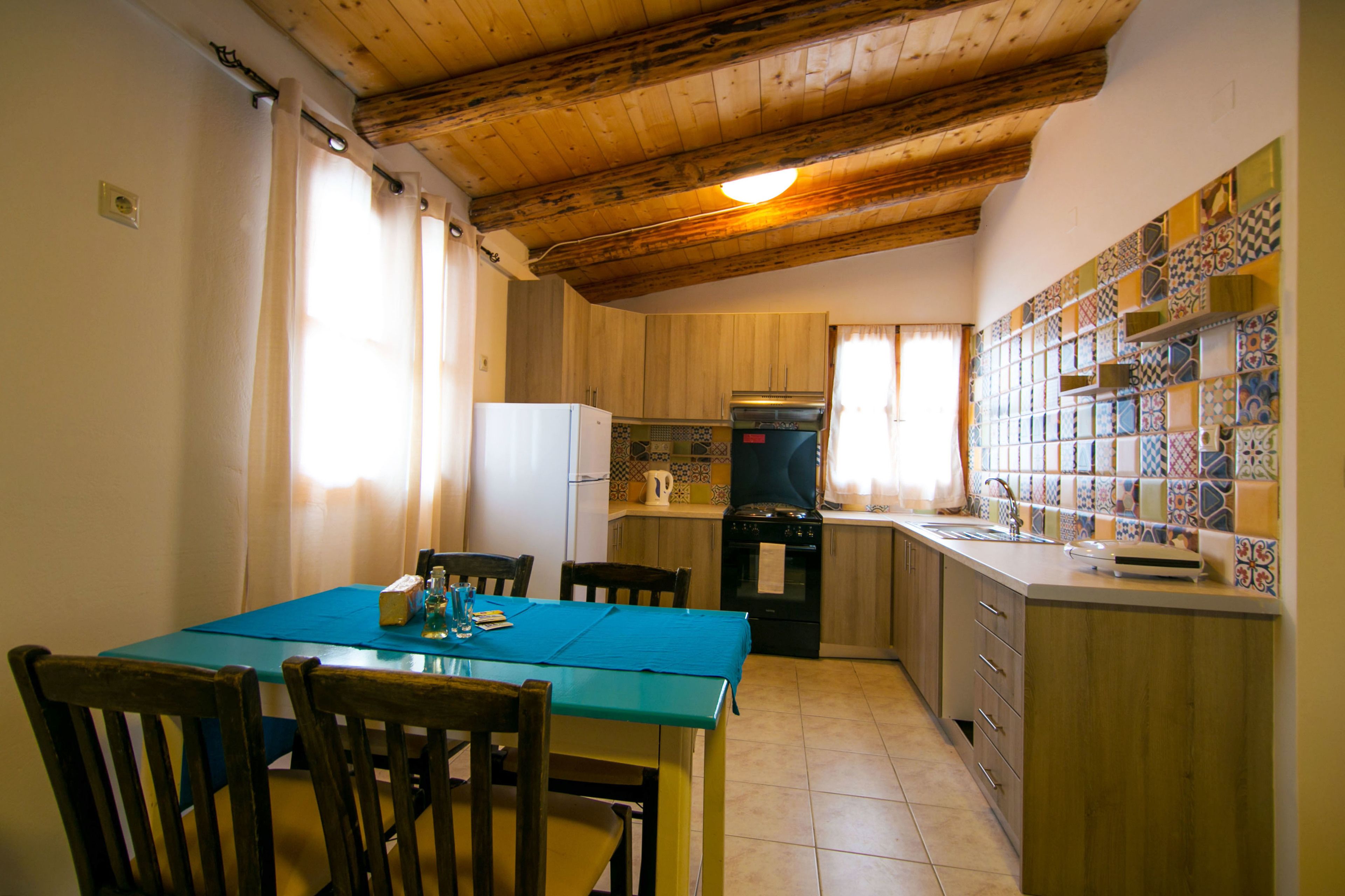 Eine Küche mit Holzausstattung, einem Esstisch mit Stühlen, einem Kühlschrank und einer gefliesten Spritzschutzleiste.