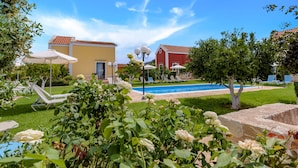 A poolside area with lounge chairs, a pool, and a garden with roses. - Athousakis Village (Chania)