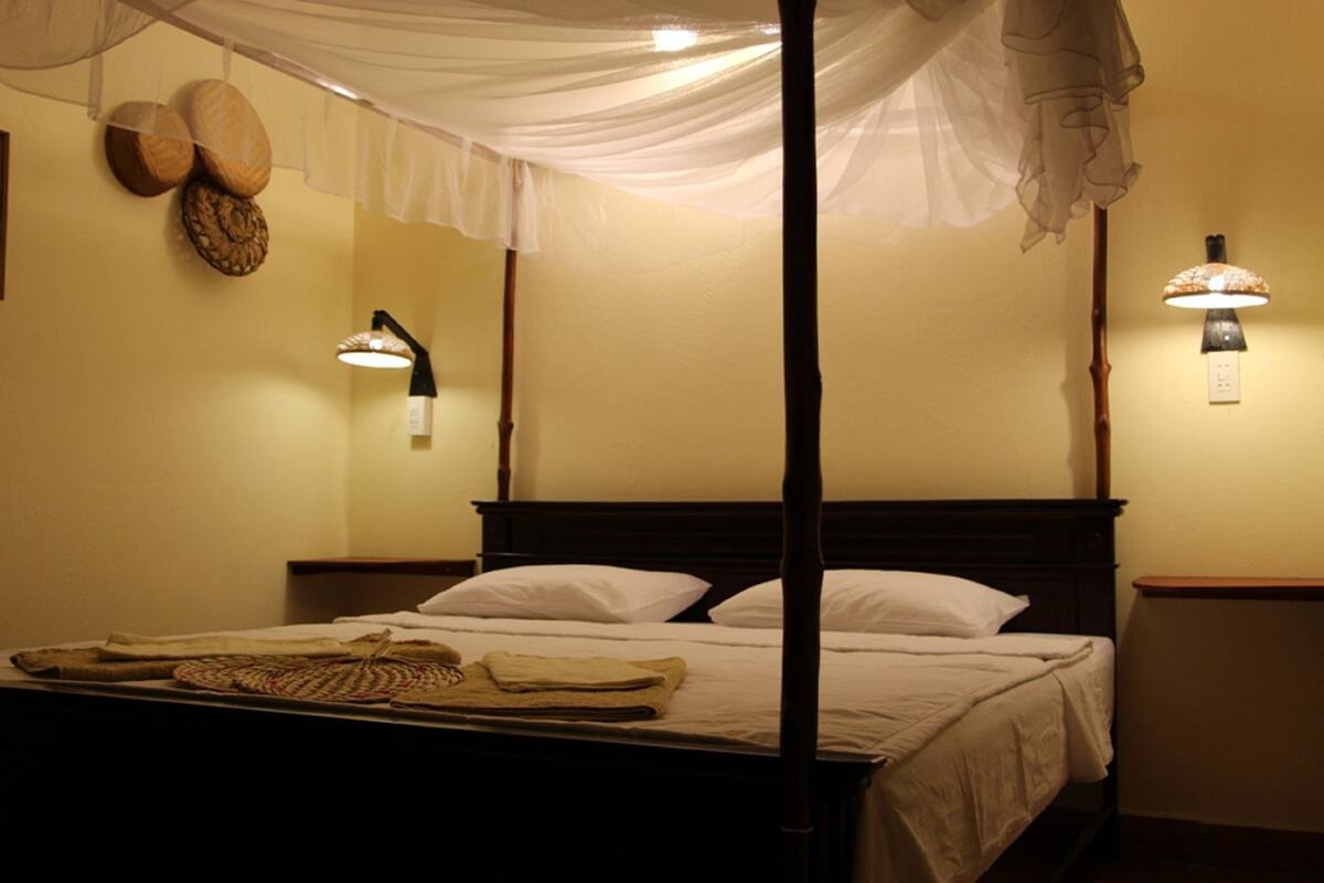 Un lit à baldaquin avec des draps blancs, un dais et deux lampes fixées au mur.