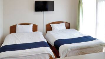 Deux lits simples avec des têtes de lit en bois, un téléviseur à écran plat fixé au mur et une fenêtre avec des rideaux verts.