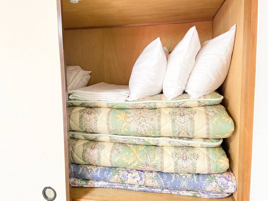Una cama con varias almohadas y una pila de mantas dobladas en un mueble de madera.