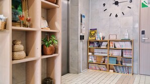 Een hal met een grote wandklok, planken met decoratieve objecten, en een boekenplank vol tijdschriften.