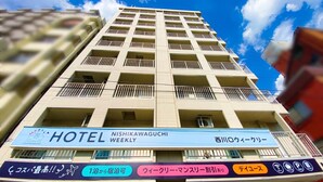 Een hotelgebouw met meerdere verdiepingen, balkons en een bord waarop staat dat het een wekelijks hotel is.