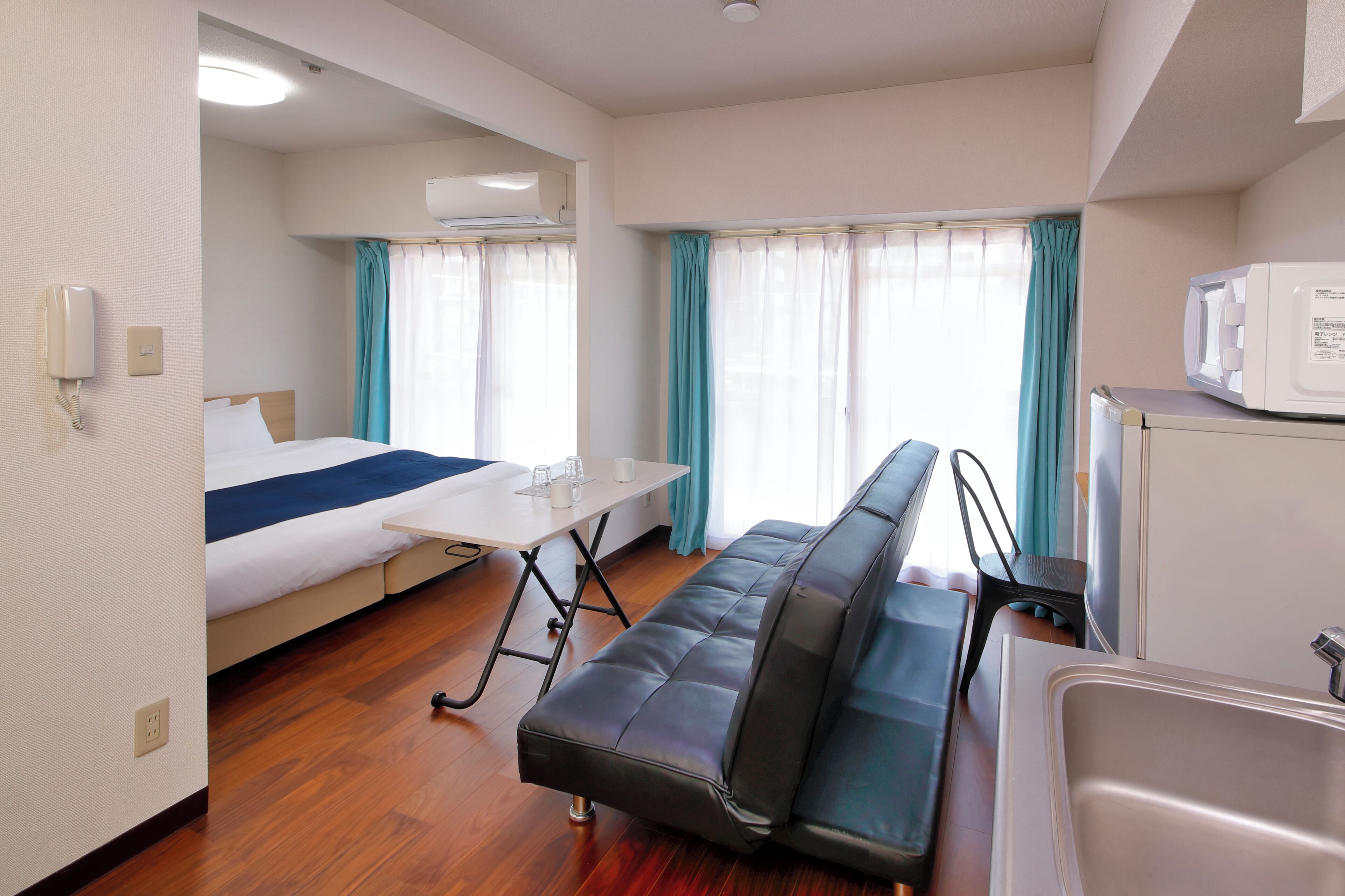 A compact hotel room with a bed, a small table, a sofa, a microwave, and a sink.