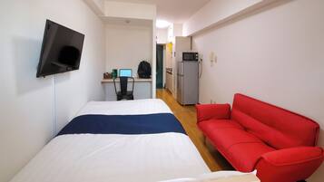 A hotel room with a bed, a red sofa, a TV mounted on the wall, a desk with a computer, and a microwave.