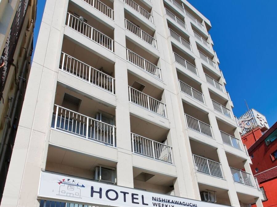Un hotel de varios pisos con balcones, una máquina expendedora de Coca-Cola y un cartel que indica que es un hotel semanal.