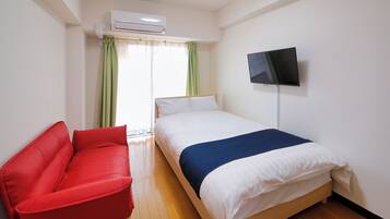 A hotel room with a bed, a red sofa, a TV on the wall, and an air conditioning unit.