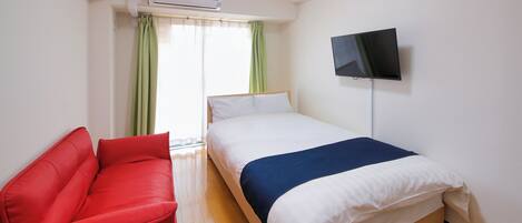 A hotel room with a bed, a red sofa, a TV on the wall, and an air conditioning unit.