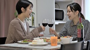 Twee personen proosten met wijnglazen aan een eettafel met diverse gerechten, een fles wijn en een kaars.