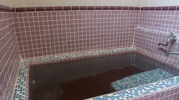 Relax in a spacious bathtub surrounded by a grid-patterned tile wall and a convenient faucet.