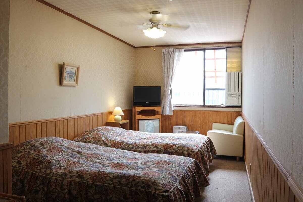A hotel room with two beds, a television, a desk, and a chair.