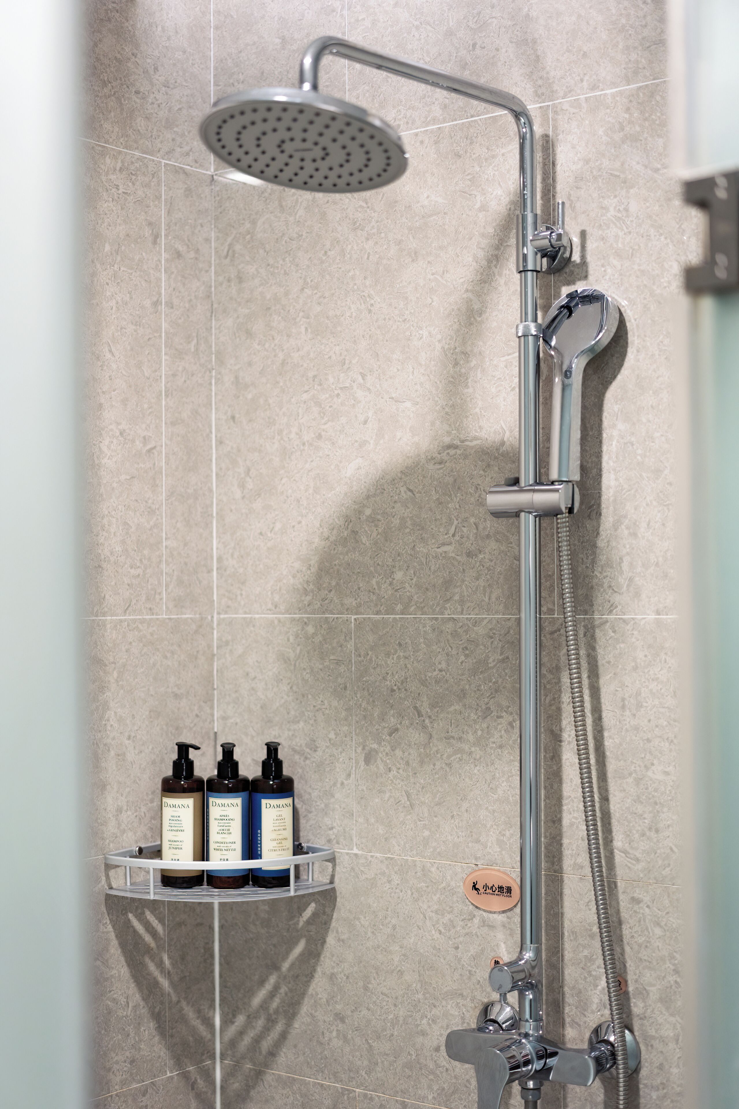 A shower with a handheld showerhead and a handheld shower hose. There are three bottles of shampoo on a shelf below the shower.