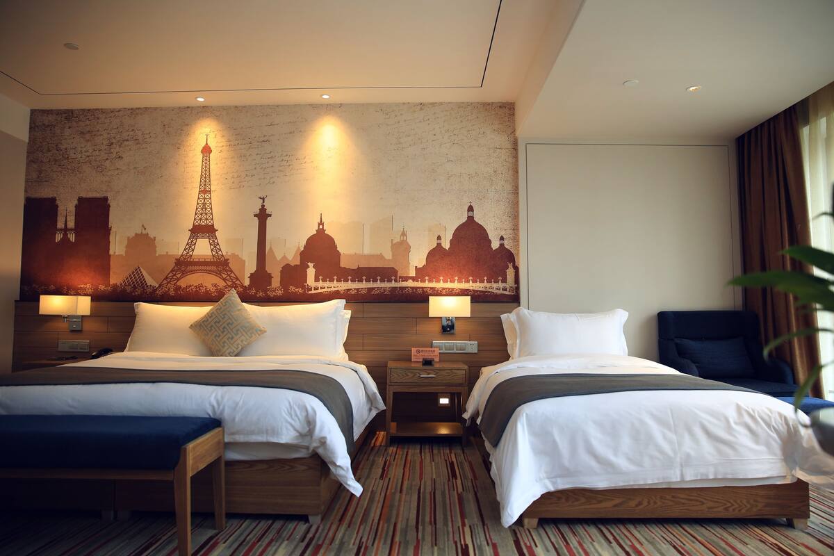 Habitación de hotel con dos camas, un mural con vista a la ciudad y un cabecero de madera.