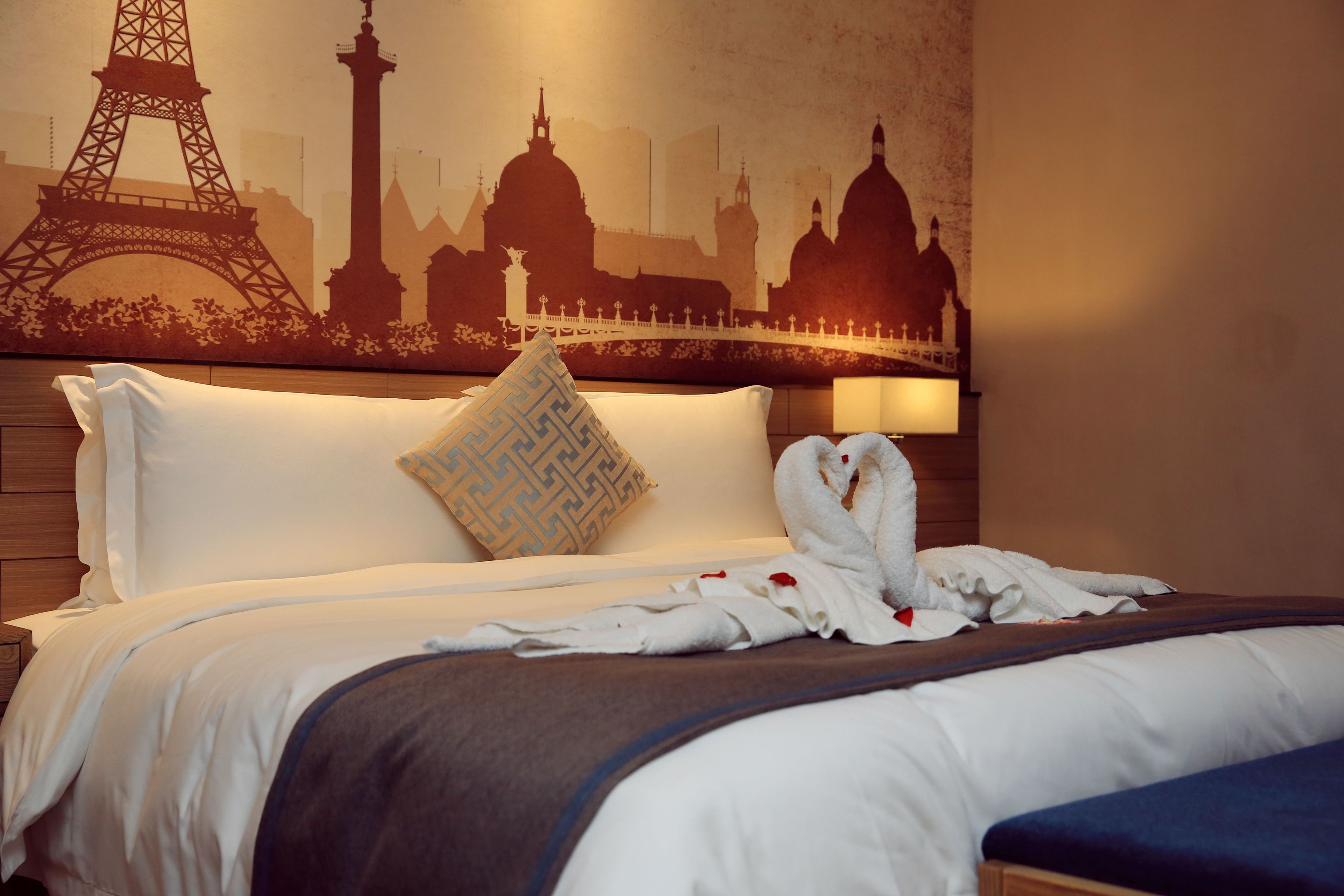 A hotel room with a bed, pillows, a blanket, and a wall mural of Parisian landmarks.