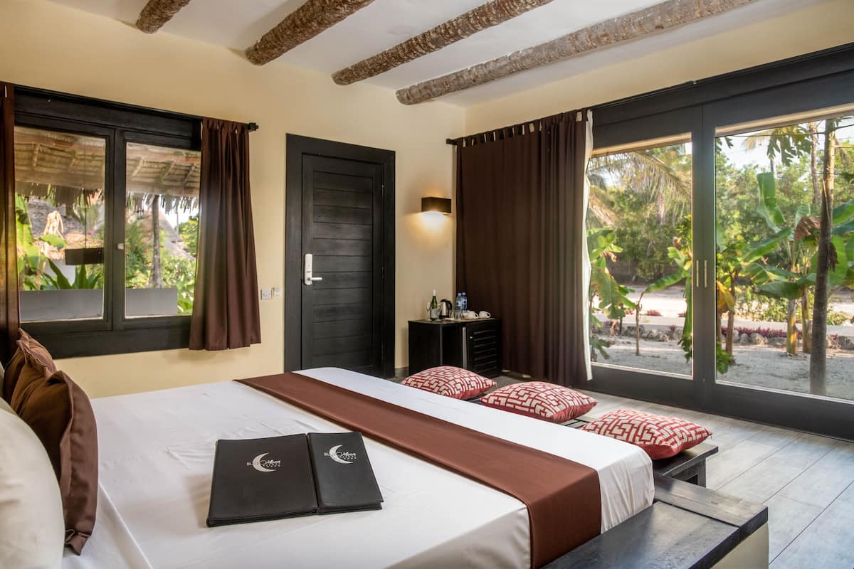Habitación de hotel con una cama grande, un escritorio con silla, una ventana con cortinas y vistas a zonas verdes.