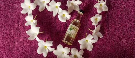 A bottle of coconut oil surrounded by white flowers on a textured purple surface.